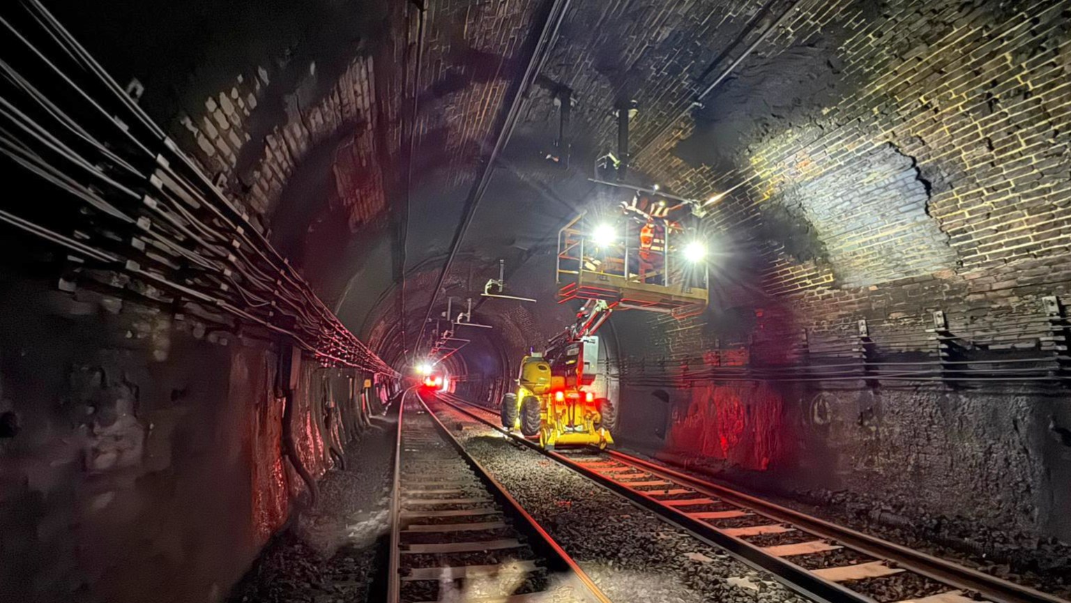Engineers working inside the Severn Tunnel on the overhead electric wiring system, with the tunnel walls visible in the background.