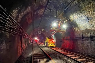 Engineers working inside the Severn Tunnel on the overhead electric wiring system, with the tunnel walls visible in the background.
