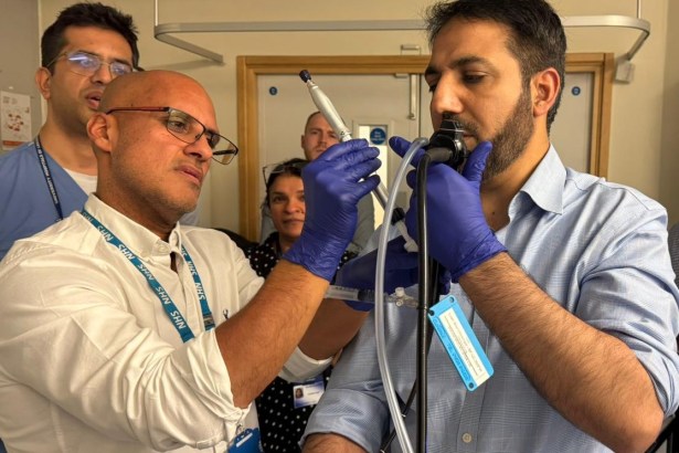 Dr Robin Ghosal wearing blue latex gloves and an NHS lanyard guides a colleague through the CryoEBUS procedure during a training session, with other medical professionals watching in the background