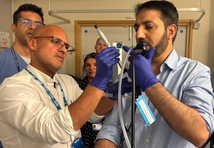 Dr Robin Ghosal wearing blue latex gloves and an NHS lanyard guides a colleague through the CryoEBUS procedure during a training session, with other medical professionals watching in the background