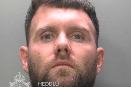 Police custody photograph of Chad White, a white man in his thirties with short dark hair and a beard, wearing a dark green top, against a grey background with a South Wales Police watermark.