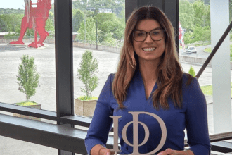 Rachael Flanagan, a woman with long brown hair wearing a blue blazer, holding a silver IoD award trophy and smiling, pictured inside ICC Wales with the large red Welsh dragon sculpture visible through the window behind her