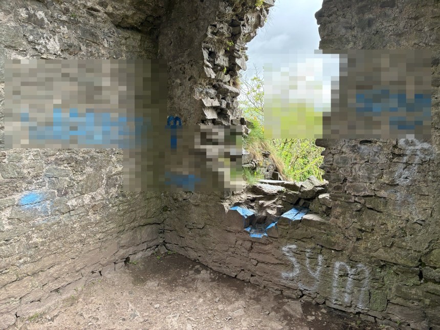 The interior walls of Castell Llansteffan showing blue spray paint graffiti daubed across the ancient stonework, with offensive language pixelated