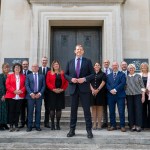 First Minister Rhun ap Iorwerth stands at the centre of a group photograph with his new Cabinet on the steps of the Welsh Government offices in Cardiff, with the Welsh Government dragon logo visible on the building behind them