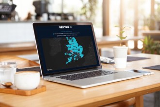 A laptop on a cafe table displaying the Reform UK votegreengetillegals.com microsite, showing a map of Great Britain with constituencies forecast to vote Green highlighted in red and labelled as prioritised for detention centres