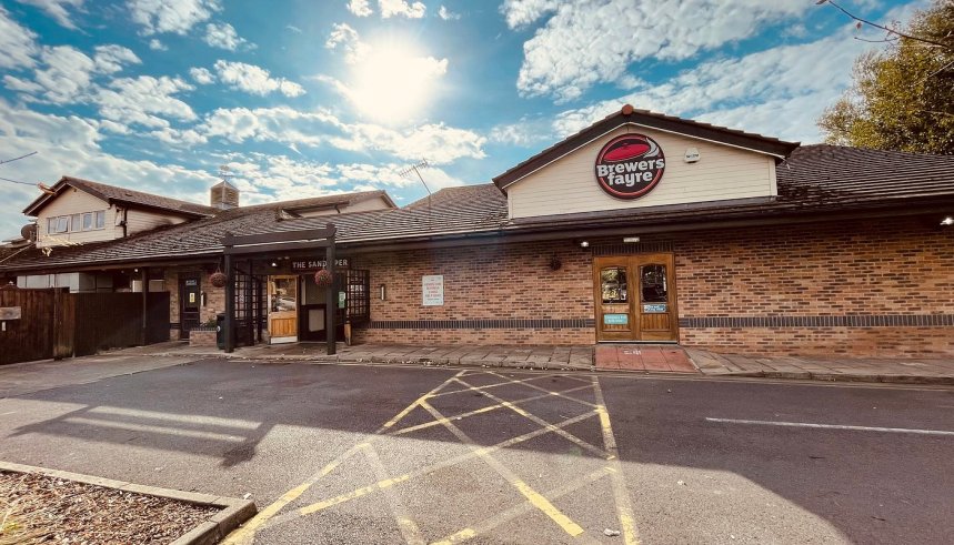 The rear entrance of the Sandpiper Brewers Fayre pub restaurant on Sandy Road in Llanelli, showing the Brewers Fayre branded fascia above the entrance, brick exterior and car park in the foreground under a sunny sky