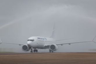 WestJet Boeing 737-8 MAX aircraft passing through a water arch created by airport fire crews as it taxis to the stand at Cardiff Airport.