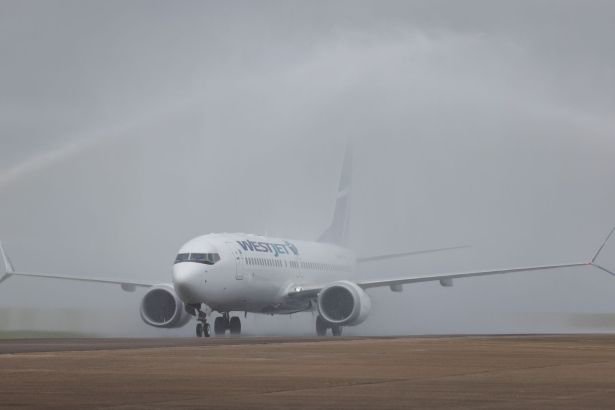 WestJet Boeing 737-8 MAX aircraft passing through a water arch created by airport fire crews as it taxis to the stand at Cardiff Airport.
