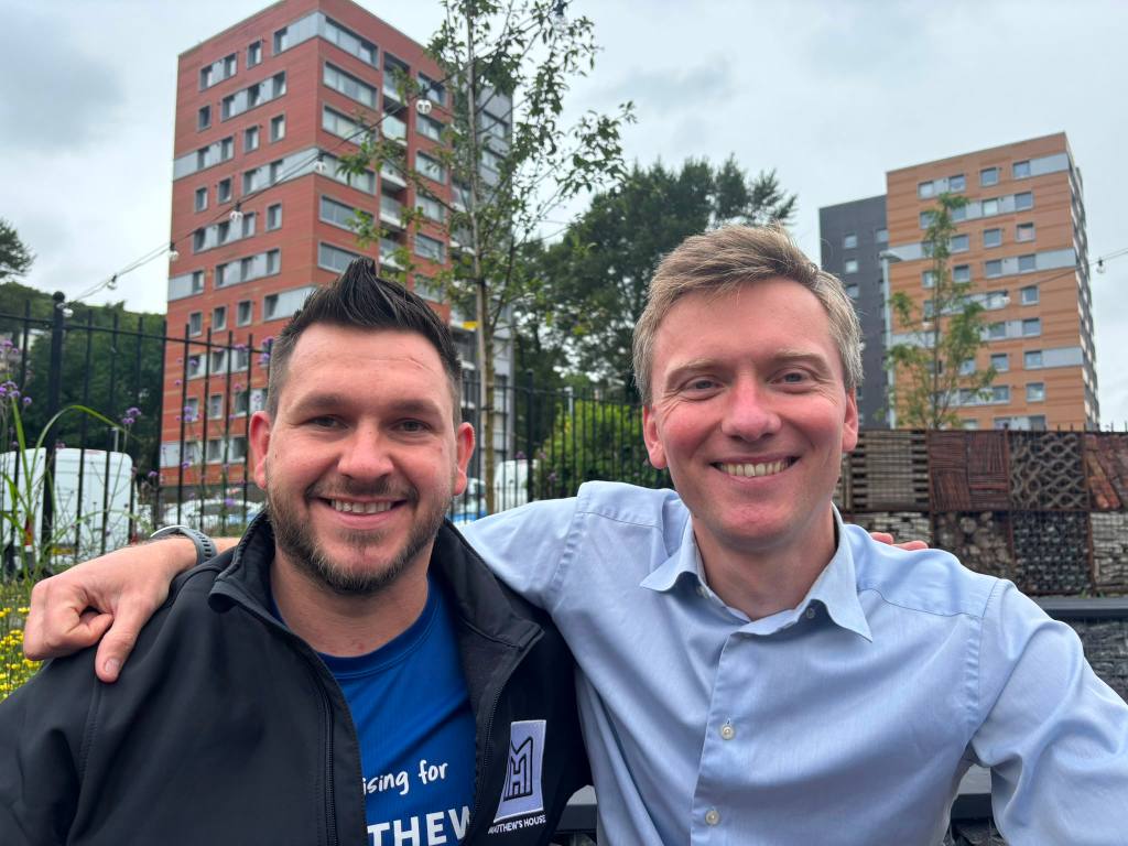 Thom Lynch and Torsten Bell with arms around each other's shoulders, smiling, with Dyfatty tower blocks behind.