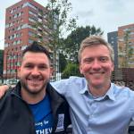 Thom Lynch and Torsten Bell with arms around each other's shoulders, smiling, with Dyfatty tower blocks behind.