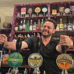 Stuart Davies stands behind the bar at the No Sign Bar on Wind Street, smiling at the camera.