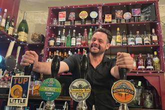 Stuart Davies stands behind the bar at the No Sign Bar on Wind Street, smiling at the camera.