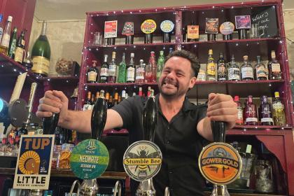 Stuart Davies stands behind the bar at the No Sign Bar on Wind Street, smiling at the camera.