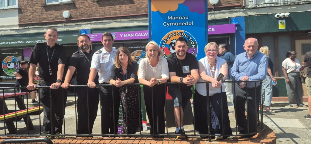 A group of people standing behind a railing outside the new Dyfatty Junction community space, with its colourful signage behind them.