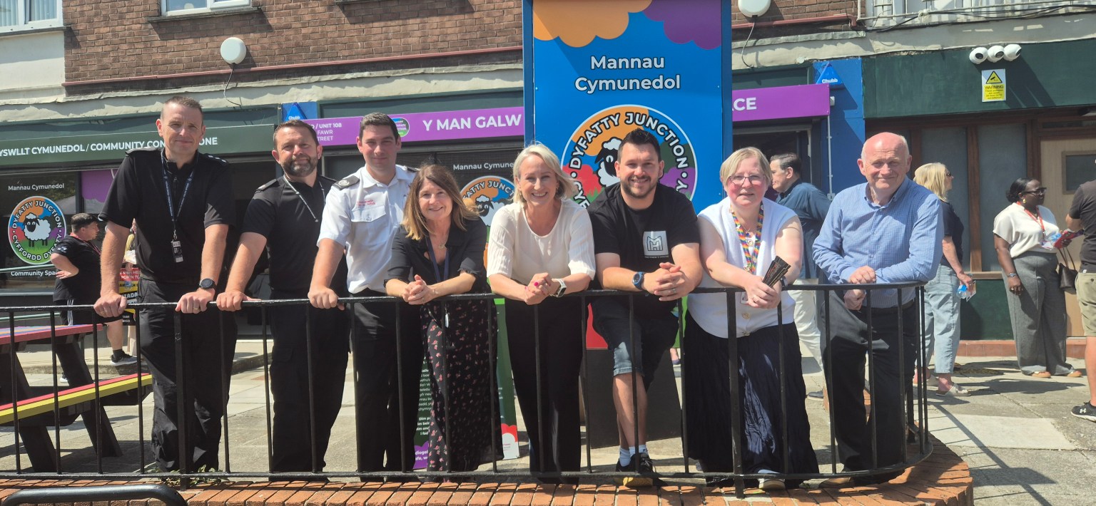A group of people standing behind a railing outside the new Dyfatty Junction community space, with its colourful signage behind them.