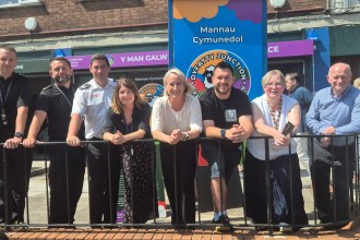 A group of people standing behind a railing outside the new Dyfatty Junction community space, with its colourful signage behind them.
