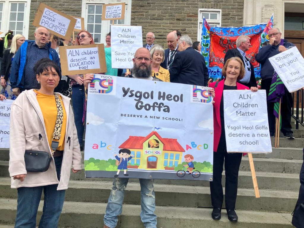 Dame Nia Griffith stands with parents and campaigners holding Ysgol Heol Goffa deserve a new school and ALN children matter placards on the steps of County Hall