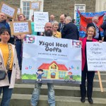 Dame Nia Griffith stands with parents and campaigners holding "Ysgol Heol Goffa deserve a new school" and "ALN children matter" placards on the steps of County Hall.