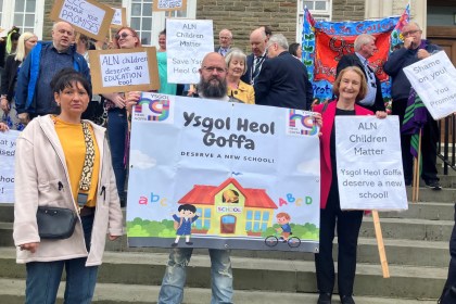 Dame Nia Griffith stands with parents and campaigners holding "Ysgol Heol Goffa deserve a new school" and "ALN children matter" placards on the steps of County Hall.