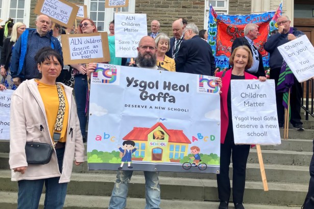 Dame Nia Griffith stands with parents and campaigners holding "Ysgol Heol Goffa deserve a new school" and "ALN children matter" placards on the steps of County Hall.