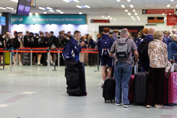 Passengers with luggage queuing at check-in desks inside Cardiff Airport, with a WestJet sign advertising direct flights to Toronto