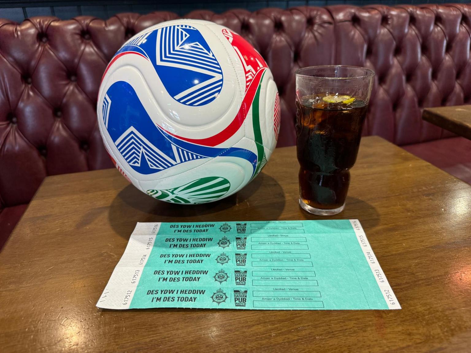 A football, a glass of cola and a sheet of bilingual DES designated driver wristbands on a pub table