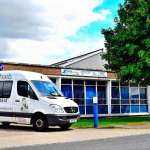 A white Doctors on Wheels Mercedes van parked outside a training centre, with signage advertising medicals for truck, bus and taxi drivers from £51.