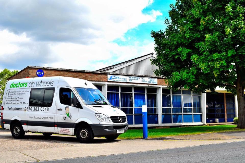 A white Doctors on Wheels Mercedes van parked outside a training centre, with signage advertising medicals for truck, bus and taxi drivers from £51.