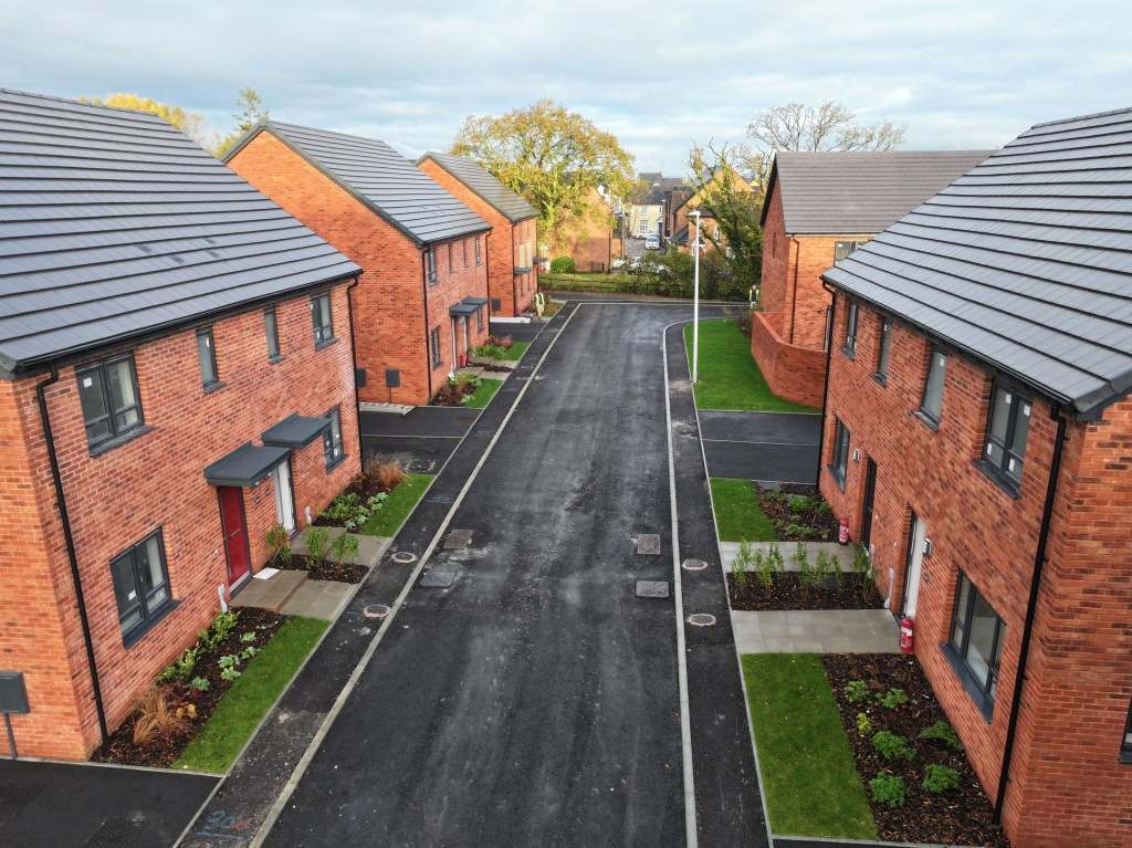 An aerial view of a new housing estate of red-brick homes with grey-tiled roofs lining a freshly laid road, on the former Gorwydd Colliery site at Woodland Grove, Gowerton.