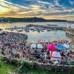 Crowds fill Tenby harbour at sunset during last year's Summer Spectacular, with stalls, a bouncy castle and boats moored in the harbour.