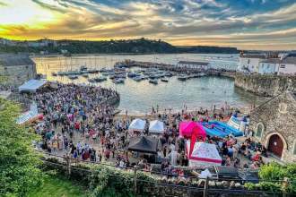 Crowds fill Tenby harbour at sunset during last year's Summer Spectacular, with stalls, a bouncy castle and boats moored in the harbour.
