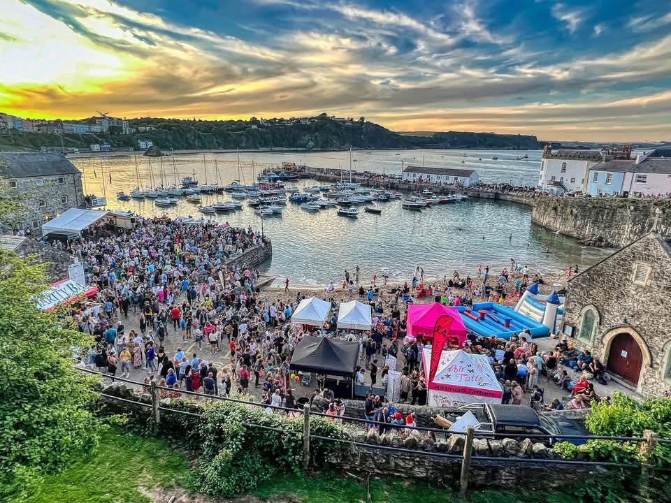Crowds fill Tenby harbour at sunset during last year's Summer Spectacular, with stalls, a bouncy castle and boats moored in the harbour.