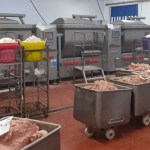 An opened plastic-lined sack of raw meat trimmings and fat in a factory cold store, beside stacked white boxes