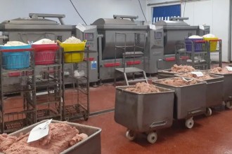 An opened plastic-lined sack of raw meat trimmings and fat in a factory cold store, beside stacked white boxes