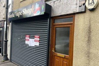 The closed grey metal shutter of World Vape Shop in Pontarddulais, with official Trading Standards closure notices taped to it.