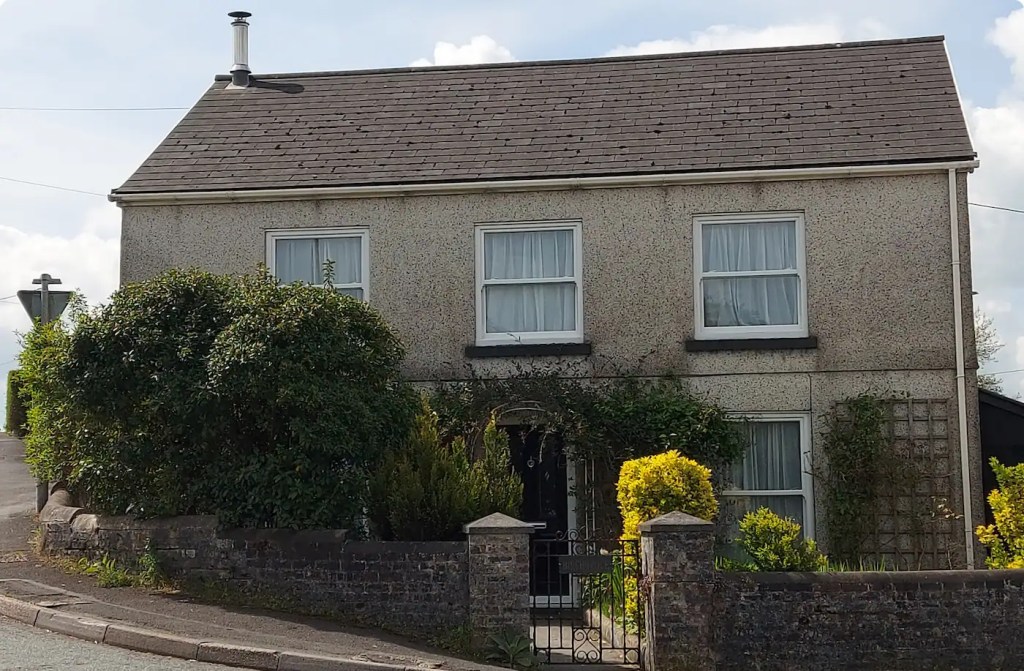 A detached stone-built house in Carmarthenshire with a heat pump flue visible on the gable end.