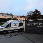 A white security van parked behind metal fencing beside a sign reading "Stradey Park Hotel", with the closed hotel buildings behind
