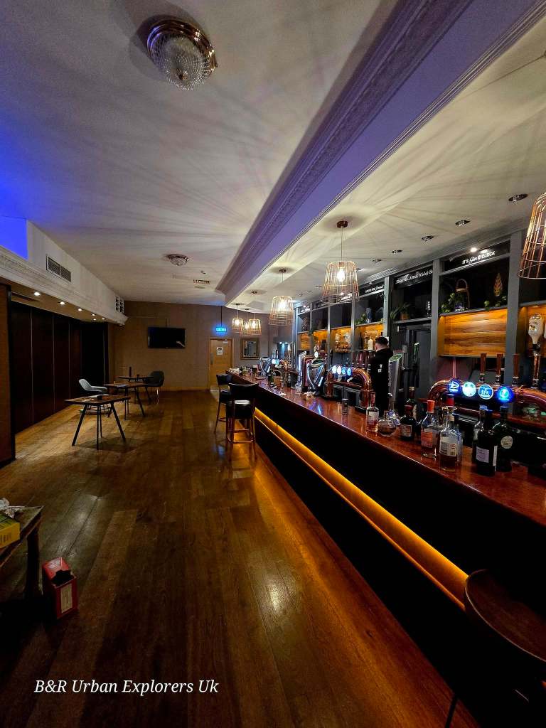 A long hotel bar lit by pendant lights with stools, optics and bottles still in position