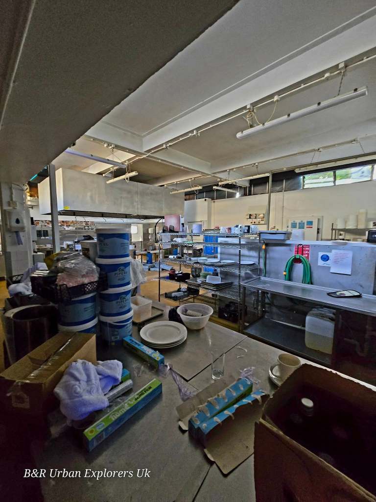 A commercial hotel kitchen with metal shelving, stacked plates and catering supplies remaining