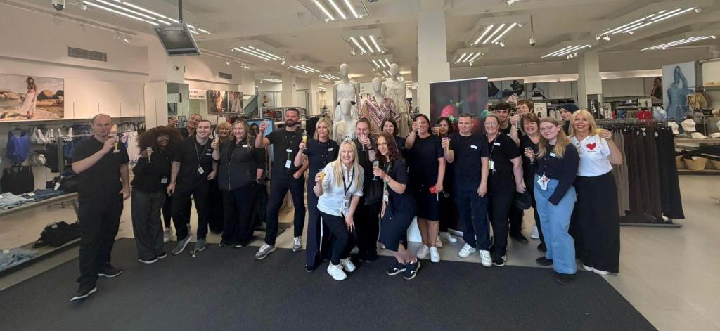 A large group of Marks & Spencer staff smiling and raising glasses inside the Swansea store on its last day