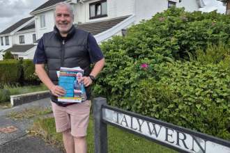 Iwan Griffiths holding Plaid Cymru campaign leaflets beside a Talywern street sign in Llangennech