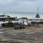 Excavators and tipper trucks working on the dug-up pitch at St Helen's, with the sea behind.