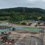 Diggers and contractor cabins on a fenced-off section of Landore Park & Ride car park, with the tree-covered slope of Kilvey Hill rising behind.