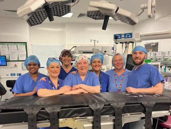 Seven members of a hospital theatre team in scrubs standing behind an operating table.