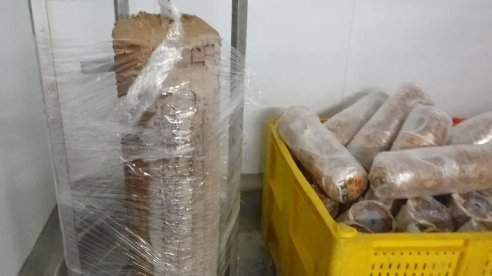 Plastic-wrapped doner kebab meat rolls stacked in a yellow crate next to a tall wrapped column of pressed meat