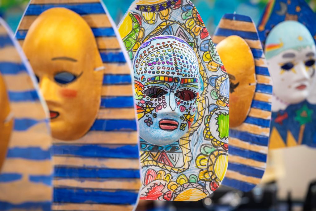 A row of brightly decorated paper Egyptian-style masks made by schoolchildren, hung on display.