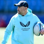 Aaron Dundon in Leinster Rugby training kit and a cap, holding a rugby ball on a pitch.