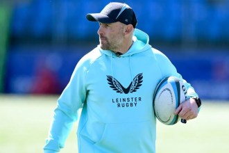 Aaron Dundon in Leinster Rugby training kit and a cap, holding a rugby ball on a pitch.