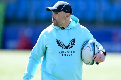 Aaron Dundon in Leinster Rugby training kit and a cap, holding a rugby ball on a pitch.