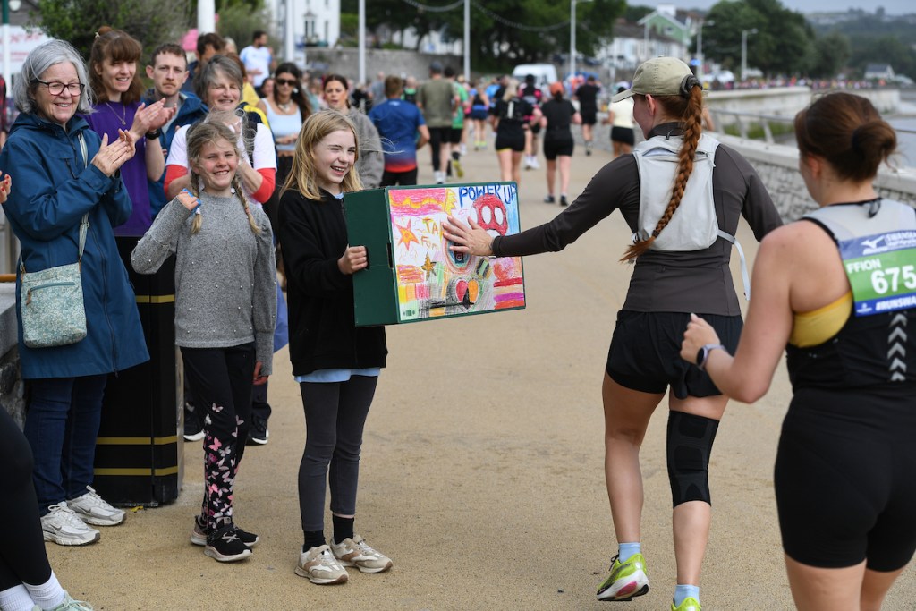 Two children holding a handmade Power Up sign for runners to touch on the seafront.